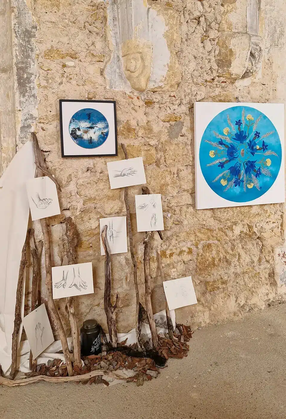 Peinture rond bleu avec fleurs en mandala, et peinture dans installation avec dessins mains, pieds, branches, écorces, céramique et dentelle