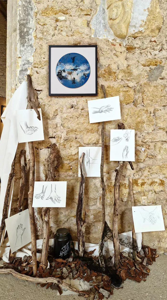 tableau rond fond bleu entre nuages et ocean, dessins de mains, branches contre le mur, écorces au sol avec céramique urne peinte et dentelle